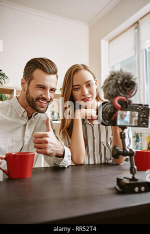 Happy bloggers. Couple of positive bloggers recording new video for their blog, bearded man showing thumbs up and smiling. Couple. Social Media. Blog. Stock Photo