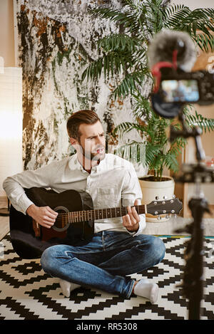 Famous singer. Bearded male music blogger playing the guitar and singing, while recording new video for his subscribers. Youtube. Music blog Stock Photo