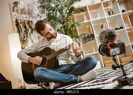 Learning guitar. Bearded male music blogger sitting on the floor at home and recording new guitar lesson for Youtube channel. Music blog. Music educat Stock Photo