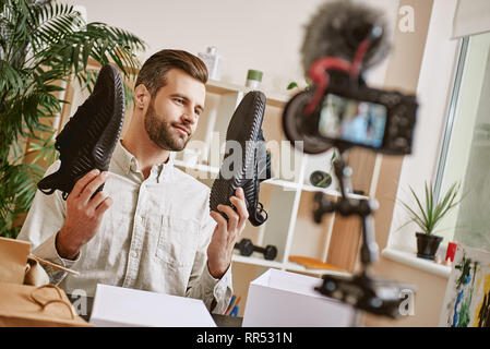 Popular fashion blogger. Young male fashion blogger holding stylish sneakers while making new content for his fashion blog. Youtube. Beauty. Video rev Stock Photo