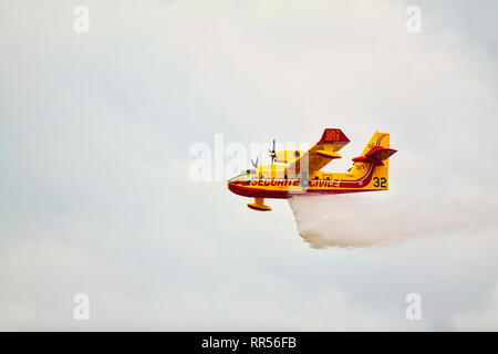 LE BOURGET, FRANCE - JUNE 24, 2017. Small yellow red seaplane hydroplane flying in the sky with clouds droping water at International aeronautical and Stock Photo