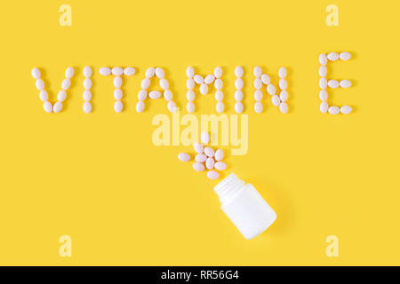 Vitamin E pills dropped from bottle on yellow background. Flat lay, top view, free copy space. Stock Photo
