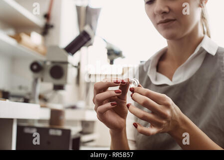 No limit to perfection. Close up of female jeweler examining the silver ring at workshop. Woman goldsmith inspecting jewelry. Stock Photo