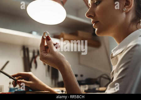 Perfection. Close up of young female jeweler looking and inspecting a ring at her jewelry workshop Stock Photo