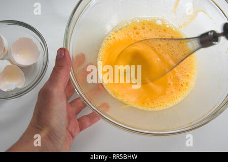 Close up view of whipped eggs in glass bowl, electric whisk and  broken empty egg shell on white background Stock Photo