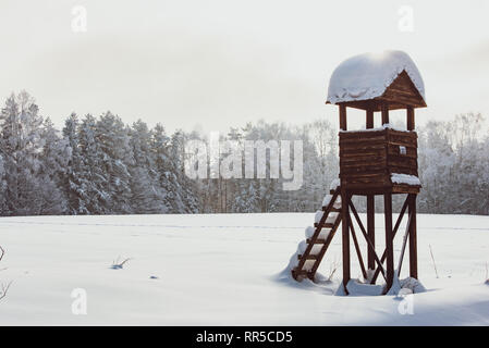 Simple wooden hunting box covered in snow. Hunting deer blind next to a row of trees in winter landscape Stock Photo