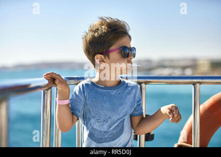 Small boy in sunglasses eating lollipop on yacht deck Stock Photo