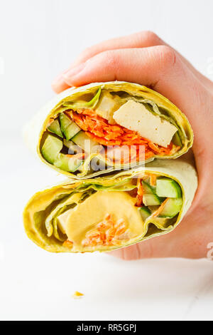 Vegan tofu wraps with cashew cheese sauce and vegetables in hand, white background. Plant based food concept. Stock Photo