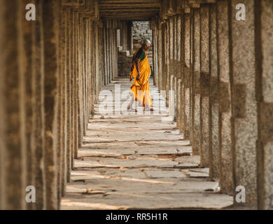 woman dressed in orange walk in the middle of temple pillars in Virupaksha Temple in hampi karnakata india Stock Photo