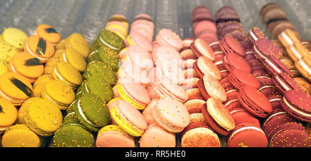 Colorful macaroons in a gift box and marshmallow in coffee cup on wooden table. Sweet macarons and flowers. Top view Stock Photo