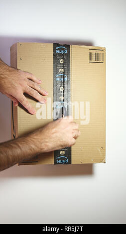 Paris, France - Feb 20, 2019: View from above of man hands unpacking new Amazon Prime cardboard box against white background Stock Photo