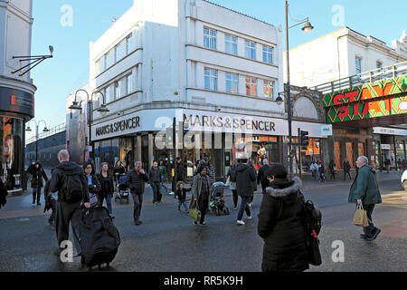 Shoppers pedestrians crossing the road at traffic lights by Marks & Spencer store on Brixton Road in Brixton, South London UK  KATHY DEWITT Stock Photo