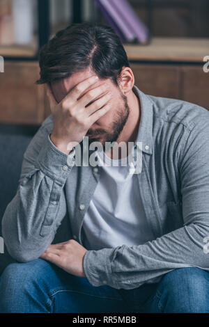 upset man sitting, crying and covering face with hand at home Stock Photo