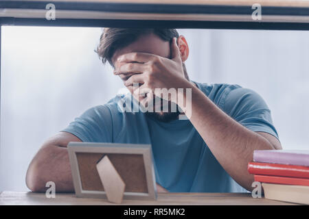 man covering face with hand and grieving near photo frame at home Stock Photo