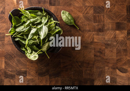 Top of view fresh baby spinach leaves in bowl on butcher board. Stock Photo