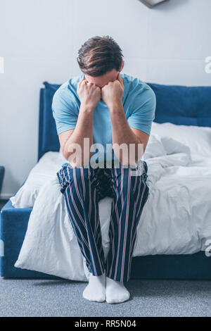 grieving man sitting on bed, covering face with hands and crying at home Stock Photo