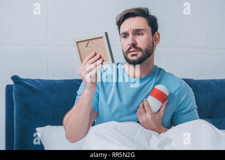 sad man lying in bed and holding photo frame with funeral urn Stock Photo