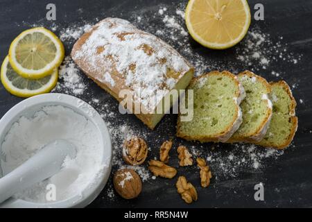 Mint cake on black surface with lemon, nuts, powdered sugar. Stock Photo
