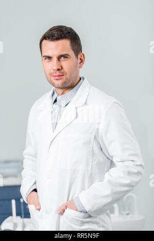 handsome dentist standing with hands in pockets in clinic Stock Photo