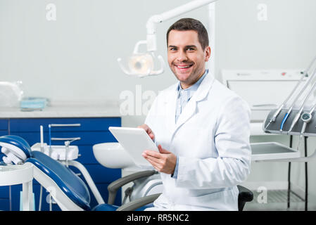 happy dentist in white coat holding digital tablet in dental clinic Stock Photo