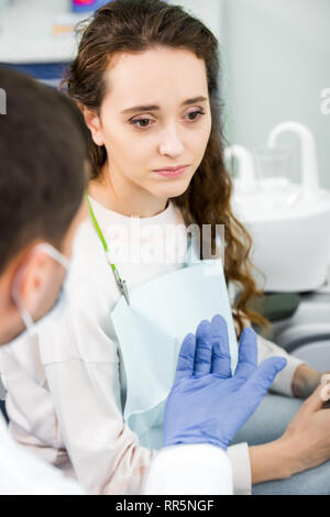 selective focus of pensive woman near dentist wearing latex gloves Stock Photo