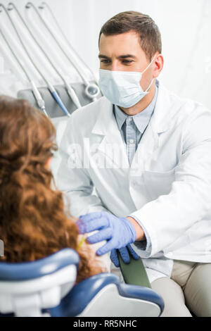 selective focus of dentist in mask putting hand on shoulder of patient Stock Photo