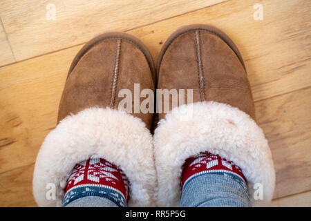 Cozy sherpa leather house slipperes with warm knit socks. Feet in slippers on wood floor. Room for copy space Stock Photo