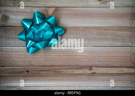 One single teal blue gift package bow on a brown wood background. Useful for birthday party or Christmas concepts and flat lay Stock Photo