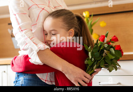 Happy Mother's Day or Birthday Background. Adorable young girl hugging her mom after surprising her with bouquet of red roses. Family celebration conc Stock Photo