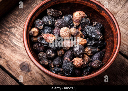 Dried red rose hips in bowl on a wooden rustic table Stock Photo