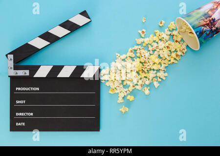 black clapperboard and a cup with scattered popcorn on a blue background Stock Photo