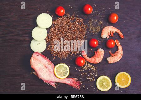 Ingredients for Indian cuisine are on a black wooden surface. The composition of the dish includes grouper fish, sliced lemon, chopped onions, brown r Stock Photo