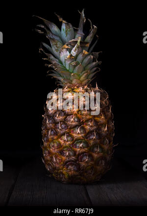Pineapple on black isolated background on old rustic desk. Stock Photo