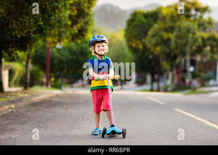 Child on kick scooter in park. Kids learn to skate roller board. Little boy skating on sunny summer day. Outdoor activity for children on safe residen Stock Photo