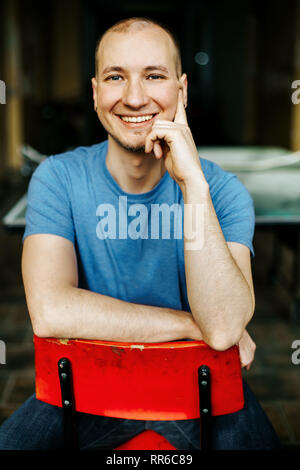 Happily smiling caucasian man in blue shirt sitting on a red chair Stock Photo