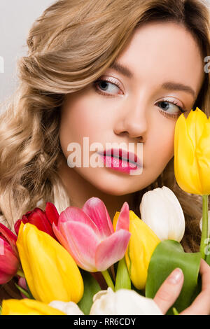 close up of young attractive spring woman holding bouquet of colorful tulips isolated on grey Stock Photo