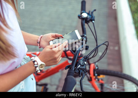 Girl is holding smartphone, searching route through application in Internet map. Against the background of red black bicycle in parking lot. Online in Stock Photo