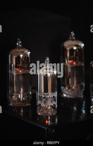 Headphone amplifier with three dominant glowing vacuum tubes / valves against a black background. Vertical / portrait aspect. Stock Photo