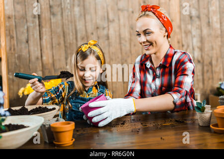 cute kid holding shovel with ground near cheerful mom with pot Stock Photo