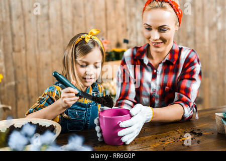 cute kid holding shovel with ground near mom with pot Stock Photo