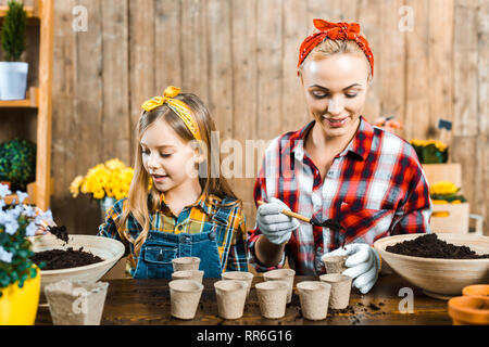 beautiful mother holding small shovel and putting ground in empty paper cup near cute daughter Stock Photo