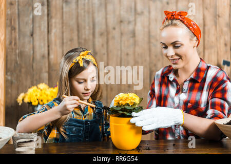 kid holding shovel with ground near pot while sitting near mother Stock Photo