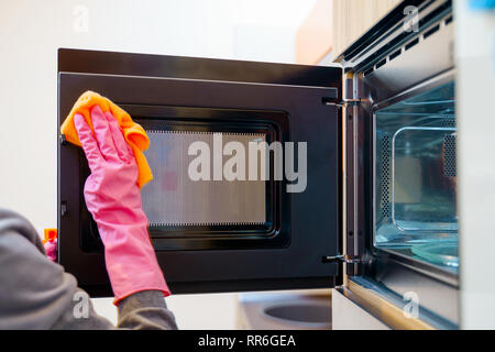 Image of woman hands in rubber gloves washing microwave. Stock Photo