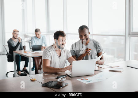 Two young businessmen using laptop and discussing new project at office, developing strategy for online business, explaining sharing ideas, preparing  Stock Photo