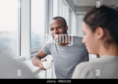 Happy African American employee have fun at coffee break in office, excited male worker laugh at colleague joke, multiracial co-workers smile negotiating. Teambuilding concept Stock Photo