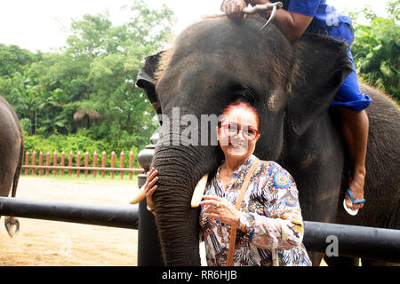 Asian thai old woman travel and posing for take photo with Elephant at garden park in Nakhon Phatom, Thailand Stock Photo