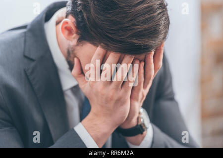 upset man in gray suit covering face with hands in room, grieving disorder concept Stock Photo