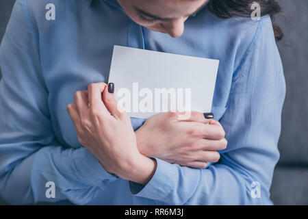 cropped view of woman in blue blouse holding and hugging photo in room, grieving disorder concept Stock Photo