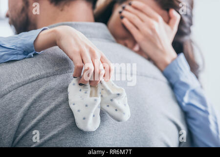 cropped view of woman, hugging man, holding baby socks and crying in room, grieving disorder concept Stock Photo
