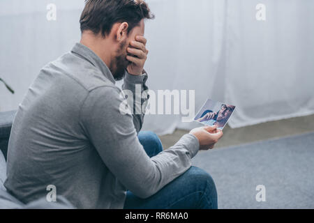 man sitting and crying while holding a male portrait at home, grieving disorder concept Stock Photo
